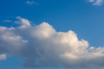 Obraz premium A bright blue sky with a large white cumulus cloud illuminated by the sun on one side. The soft texture of the clouds creates a sense of space, harmony, and freshness on a fine day.
