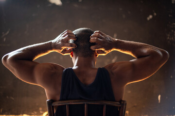 Man sitting with hands on head, backlit, wearing a dark tank top. © Rawpixel.com
