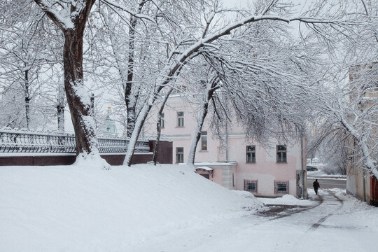 View of a snow-covered street with bare trees, a pink historic building, and a person walking in winter Moscow, Moscow, Russia.