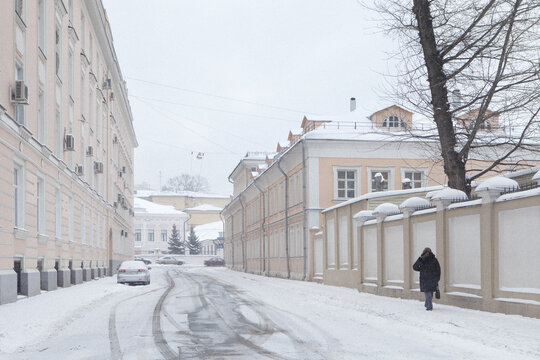 View of a snowy street lined with historic pastel-colored buildings and a person walking along a snow-covered sidewalk in Moscow, Moscow, Russia.