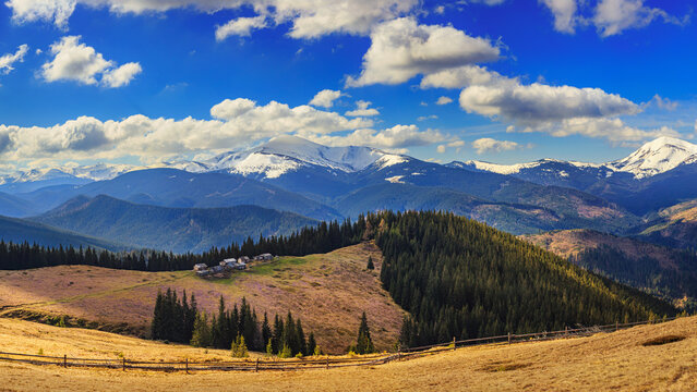 Shepherd dwellings and spring meadows of Hryhorivka Polonyna seen from a hiking path on Kukul Ridge, featuring the Chornohora mountains of the Ukrainian Carpathians in the background.