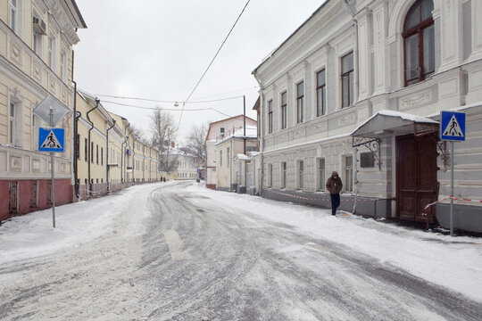 View of a snow-covered street lined with historic neoclassical buildings and a lone pedestrian walking past a doorway in Moscow, Moscow, Russia.