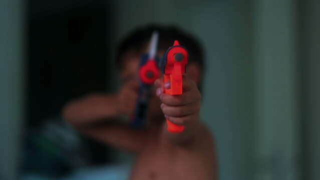 Young boy aiming colorful toy blasters toward camera during imaginative indoor play capturing childhood fantasy, excitement and playful pretend action at home
