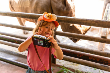 Child taking a photo of a rhinoceros at a zoo, wearing a cap. © Rawpixel.com