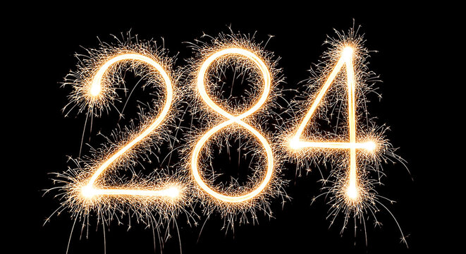 Dramatic firework explosion creating the year '284' against a black night sky, glowing with bright sparks and golden light effects.