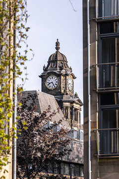 View of the historic clock tower of Lancaster Town Hall framed by modern architecture and spring foliage under a clear sky Lancaster, England, United Kingdom.