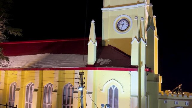 illuminated gothic church tower at night with clock face and architectural details in shimla
