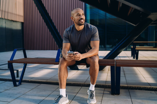 Smartphone held by athlete against blurred city background, person checking notification or fitness app after training, mobile connection and digital lifestyle, authentic representation, copy space.