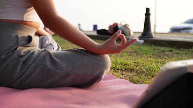 Close up Asian woman hands performing lotus pose in meditation, focusing on breath control in morning park. Hands person practicing yoga while sitting on yoga mat with sunrise for concept wellness 