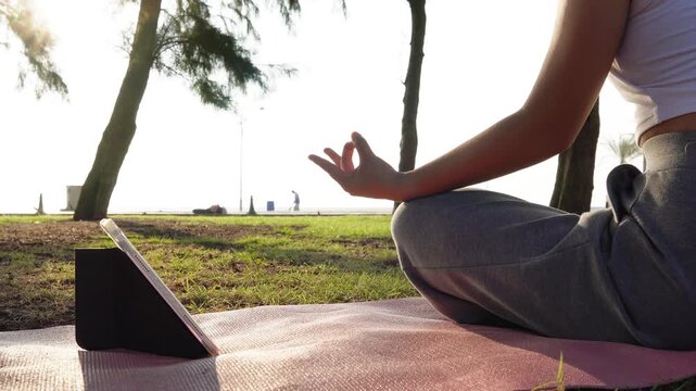 Close up Asian woman hands performing lotus pose in meditation, focusing on breath control in morning park. Hands person practicing yoga while sitting on yoga mat with sunrise for concept wellness 