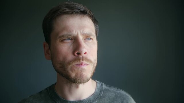 Handsome caucasian man with beard slowly eating single potato chip, savoring taste, crunch while standing in front of plain gray background in studio setting. Caucasian man eating potato chips