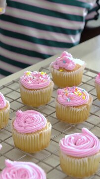 Vertical video: Entering hand in striped tee sprinkling onto cupcakes on rack, adding piped topper