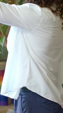 Vertical video: Spotting trailing plant, adult reaching and caring for shelf at home in white shirt
