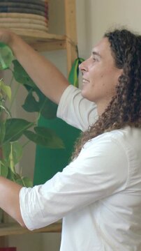 Vertical video: Reaching adult in white shirt sleeves rolled watering plant on rack with green can