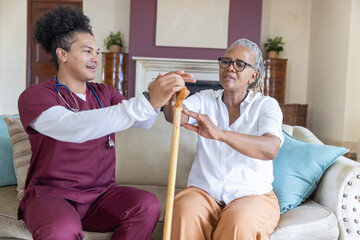 Obraz premium Senior African American woman reaching for cane, caregiver holding handle with stethoscope at home