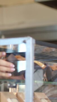Vertical video: Reaching right hand pulling white cup from glass display at bakery, metal frame