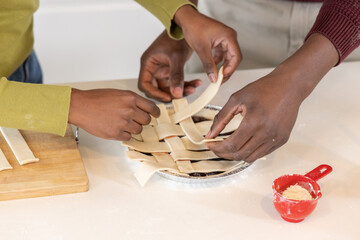 African American friends weaving lattice over fruit pie in aluminum tin, red measuring cup visible © wavebreak3