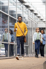 Obraz premium Diverse commuters walking along glass walkway, man holding coffee cup wearing mustard sweater