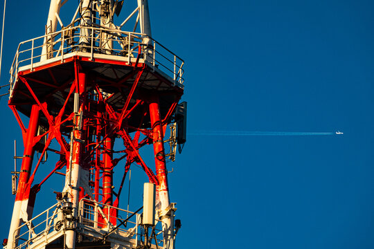 Telecommunication tower close up with airplane flying in blue sky