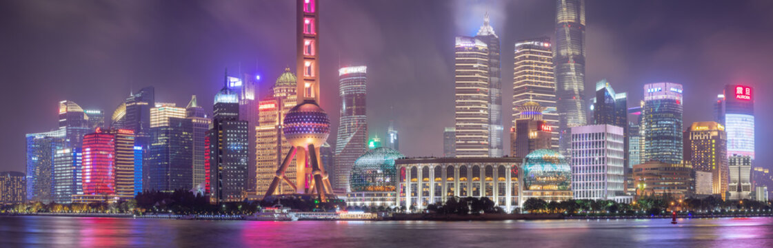 View of the illuminated Pudong skyline with the Oriental Pearl Tower and skyscrapers reflecting in the Huangpu River at night in Shanghai, Shanghai, China.