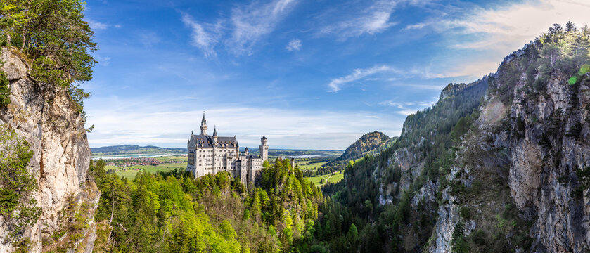 Tourists enjoy the view of Schloss Neuschwanstein, a famous castle in Bavaria, Germany, surrounded by trees and fields.