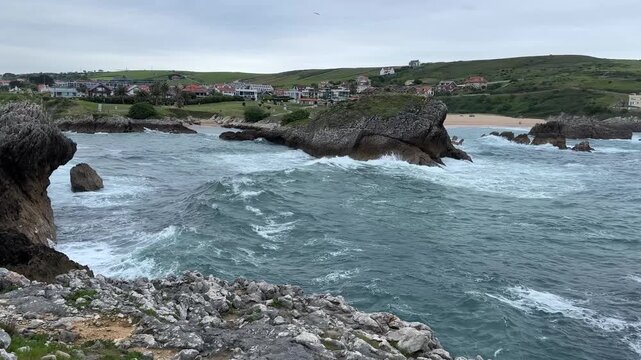 Camera following a rolling wave of cold gray Atlantic water through a rocky bay toward weathered coastal rocks.