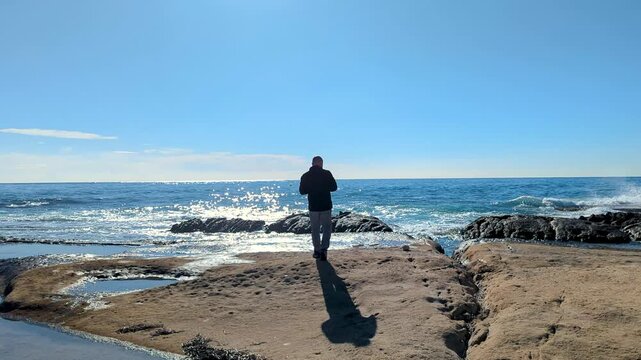 Photographer exploring angles to compose sea birds by reflection pools on the rocky coast of San Juan bay in Alicante Spain in 4k at 50 fps