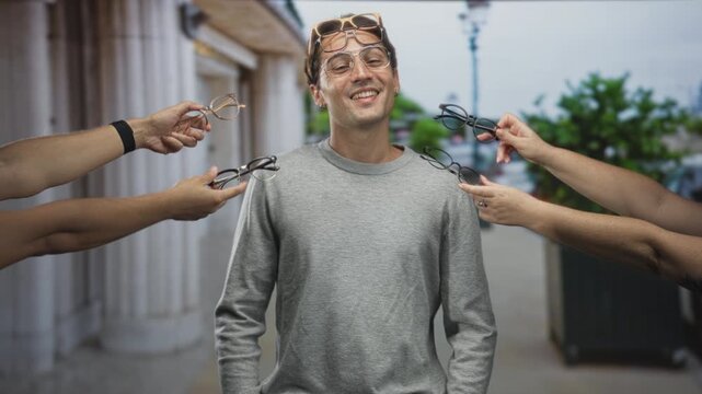 Man smiling with sunglasses on forehead as multiple hands offer eyeglasses on a city street; confidence choice.