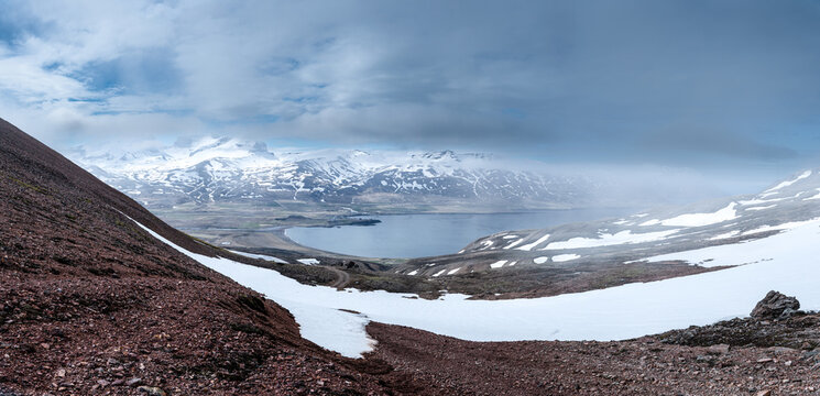 View of Borgarfjordur eystri fjord with snow-capped mountains and the coastal village under a cloudy sky Bakkagerdi, Mulathing, Iceland.