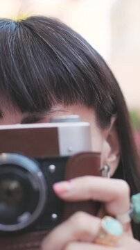 vertical shot. Close-up of a dark-haired woman holding a vintage camera near her face, looking through the viewfinder with focused expression. girl with a camera.