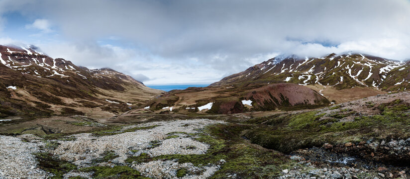 View of the rugged Brunavik valley with patches of snow on the mountains and mossy slopes under a cloudy sky in Bakkagerdi, Mulathing, Iceland.