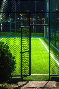 View of an illuminated artificial turf sports court seen through an open chain-link fence door at night in Rio de Janeiro, State of Rio de Janeiro, Brazil.