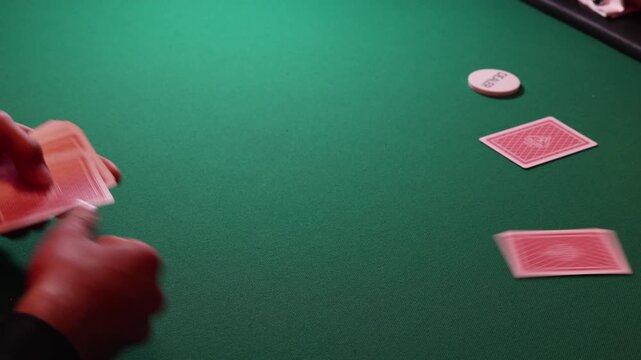 A dealer moves a card across the poker table while several red backed cards lie on the green surface. The dealer chip is positioned near the center, and the motion blur indicates an ongoing deal. 