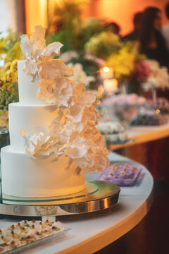 View of a three-tier white wedding cake decorated with delicate sugar flowers on a dessert table with floral arrangements Rio de Janeiro, State of Rio de Janeiro, Brazil.