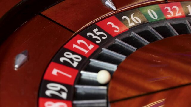 Roulette wheel in motion with a ball resting in the 7 pocket. The circular track contains alternating red and black numbered fields separated by metal dividers on a polished wooden surface. 