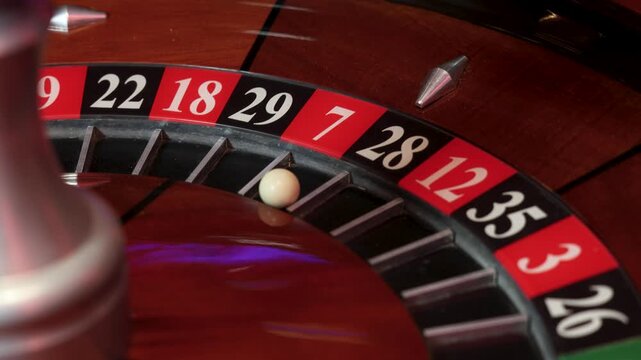 A roulette wheel rotates around its central spindle while a white ball settles in pocket 7. The numbered pockets form a circular pattern with metal separators and a polished wooden track. 