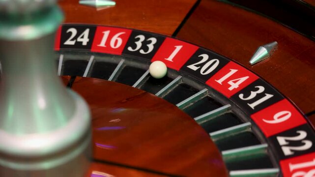 A roulette wheel turns around its central spindle while a white ball rests in pocket 1. The numbered pockets form a circular sequence with metal separators set into a polished wooden track. 