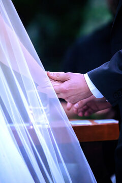 View of a bride and groom holding hands during a wedding ceremony with a white veil in the foreground Rio de Janeiro, State of Rio de Janeiro, Brazil.