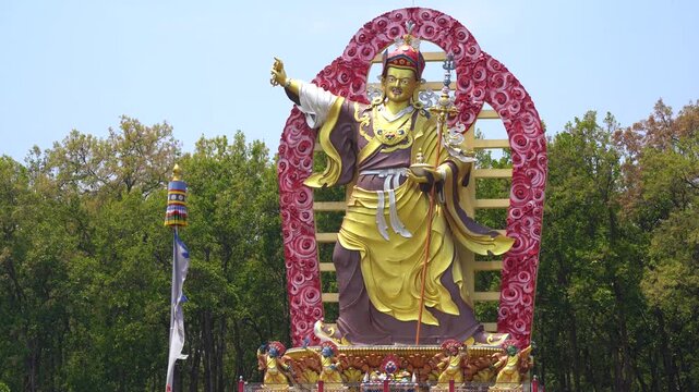 Locked shot showing the great statue of Guru Padmasmabhava, Guru Dregpa Kundul the tamer showing Rinpoche in wrathful form surrounded by prayer flags and trees in Dehradun Mindrolling Monastery