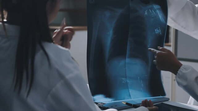 Brunette female clinician in lab coat pointing at laptop screen while making presentation of medical data to group of intercultural colleagues