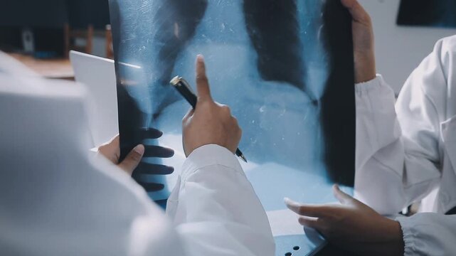 Brunette female clinician in lab coat pointing at laptop screen while making presentation of medical data to group of intercultural colleagues