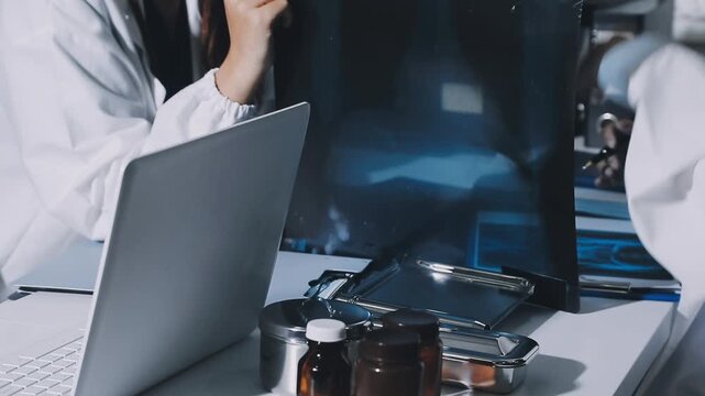 Brunette female clinician in lab coat pointing at laptop screen while making presentation of medical data to group of intercultural colleagues