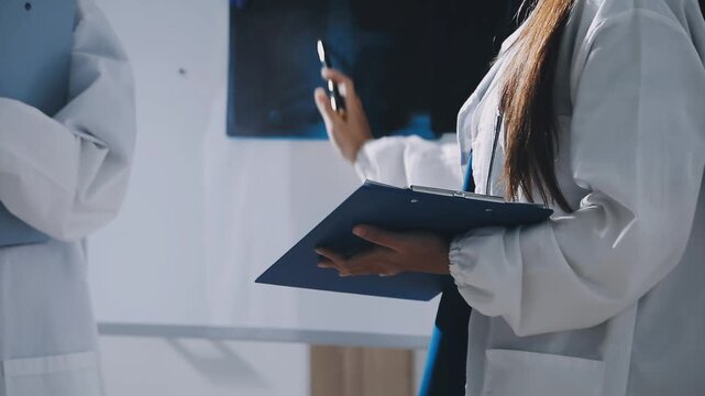 Brunette female clinician in lab coat pointing at laptop screen while making presentation of medical data to group of intercultural colleagues