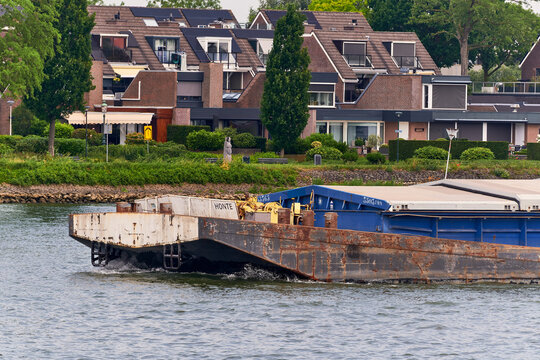Dordrecht, Netherlands - 31 May 2026: View of the bow of a pusher tug barge with a closed cargo hull navigating the Oude Maas river past residential houses.