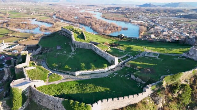 Aerial drone camera moving forward and tilting down over Rozafa Castle in Shkod&euml;r, Albania, focusing on the inner green courtyards, defensive stone walls, and Lead Mosque