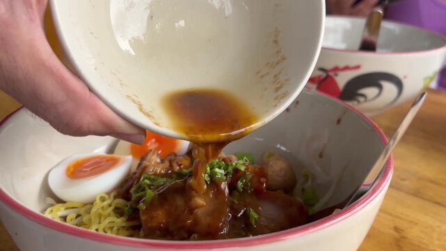 The broth is poured into a bowl with Thai noodles and pork.