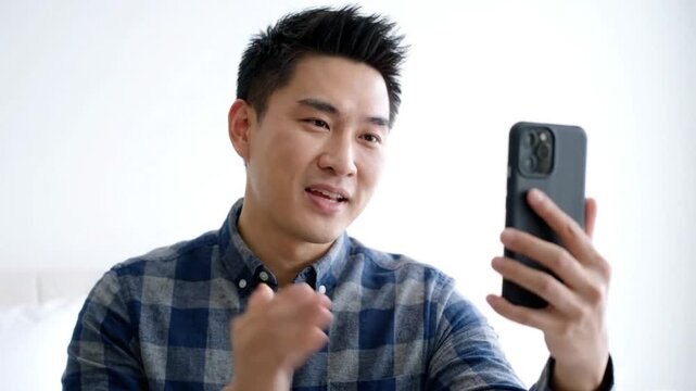 Young asian man having a video call on his smartphone, expressing sincerity and excitement