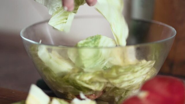 Close Up of Hand Throwing and Dropping Fresh Cut Iceberg Lettuce Salad into Bowl