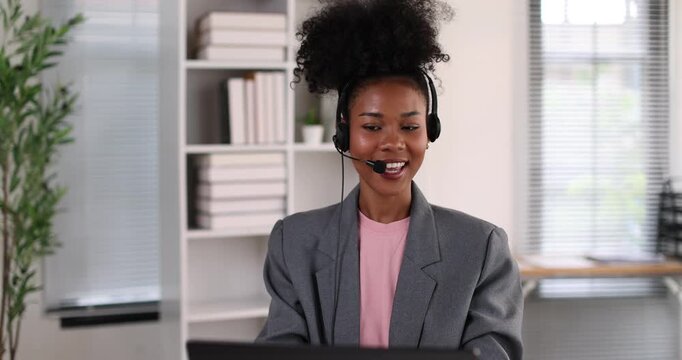 African american businesswoman smiling, wearing a headset with a microphone, providing online assistance and support while working from her home office setup