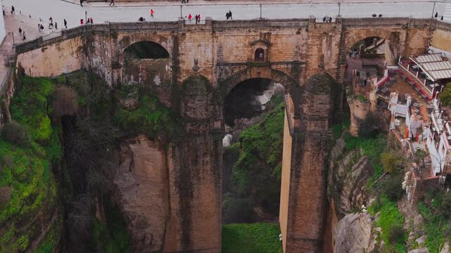 Ronda, Spain - 08 feb 2026: Aerial view of the Puente Nuevo bridge spanning the El Tajo gorge with people walking across and lush green vegetation on the cliffs.